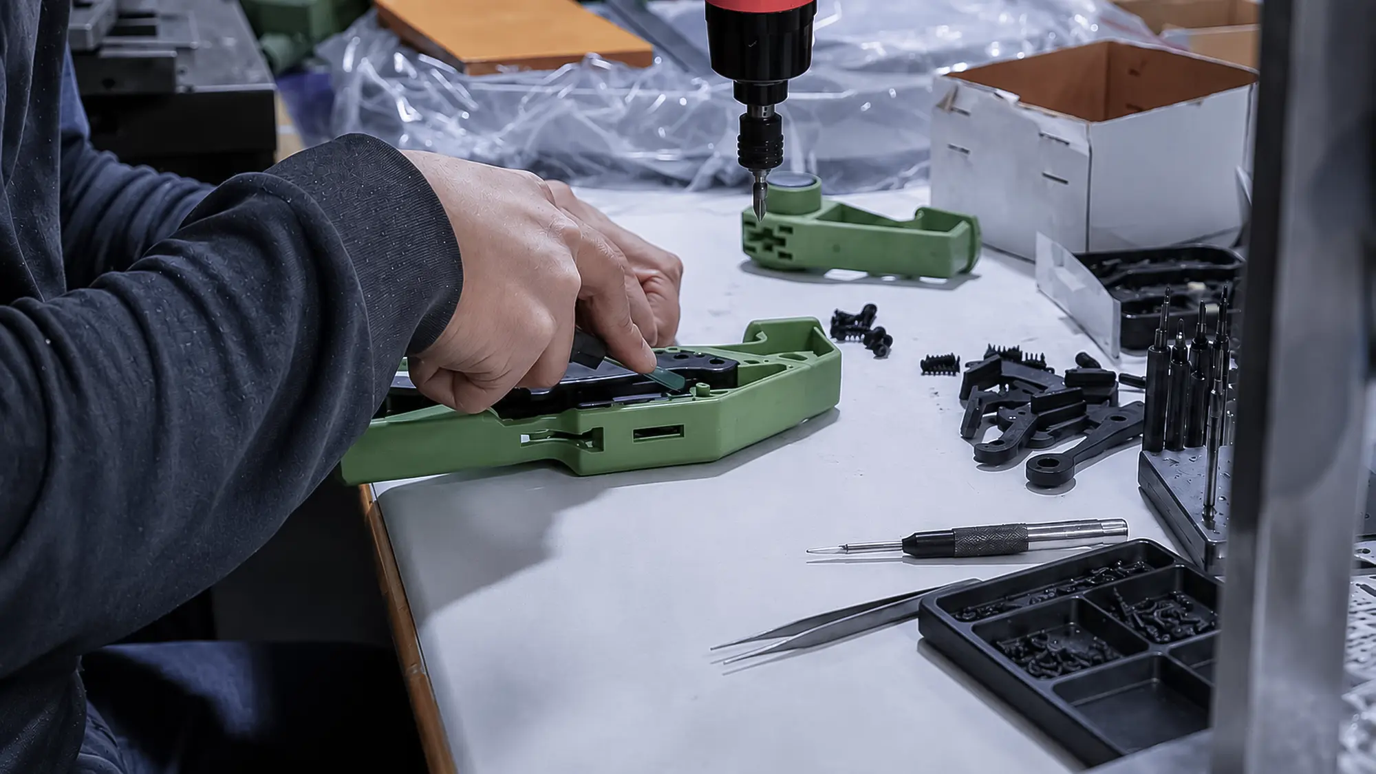 Worker assembling PCB, wiring, connectors, battery, and mechanical components into a product using fixtures and controlled tools
